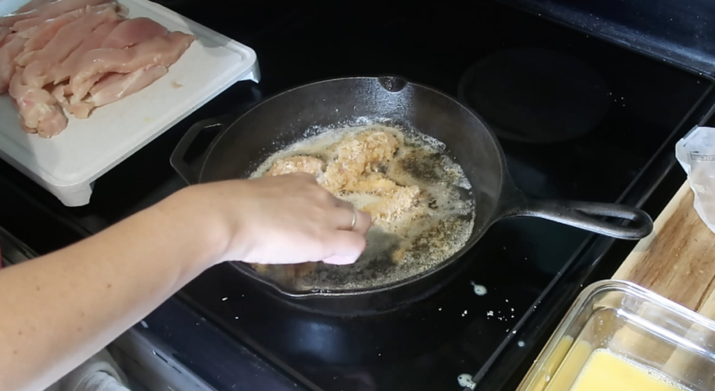 lady frying carnivore chicken strips in a cast iron skillet