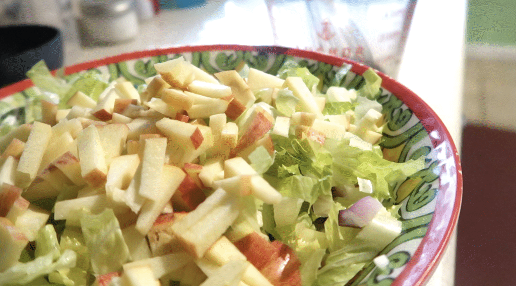 red rim bowl with salad inside an maple balsamic vinaigrette in a jar in the background