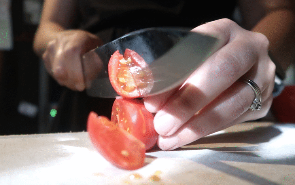 up close of a woman's hands chopping tomatoes with a sharp knife