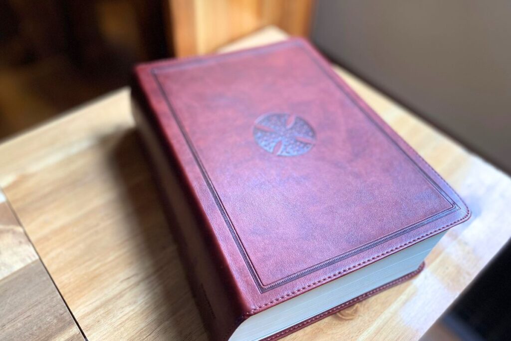 brown leather bible with a dark brown cross on the front sitting on a wood bench