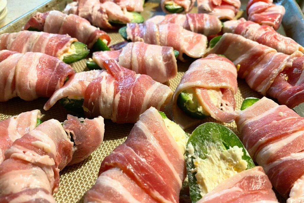 uncooked bacon wrapped jalapeños stuffed with cream cheese on a pan