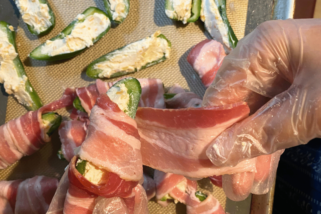 close up shot of woman wrapping half a jalapeño stuffed with cream cheese with a piece of bacon