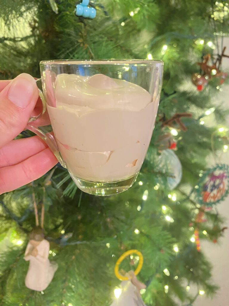 small glass espresso cup with easy carnivore dessert coffee whip inside of it, in front of a Christmas tree