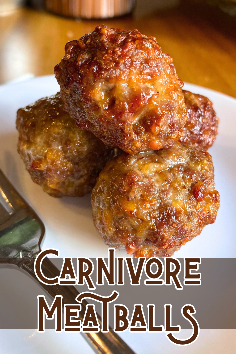 close up pile of 4 meatballs on a white plate with a silver fork