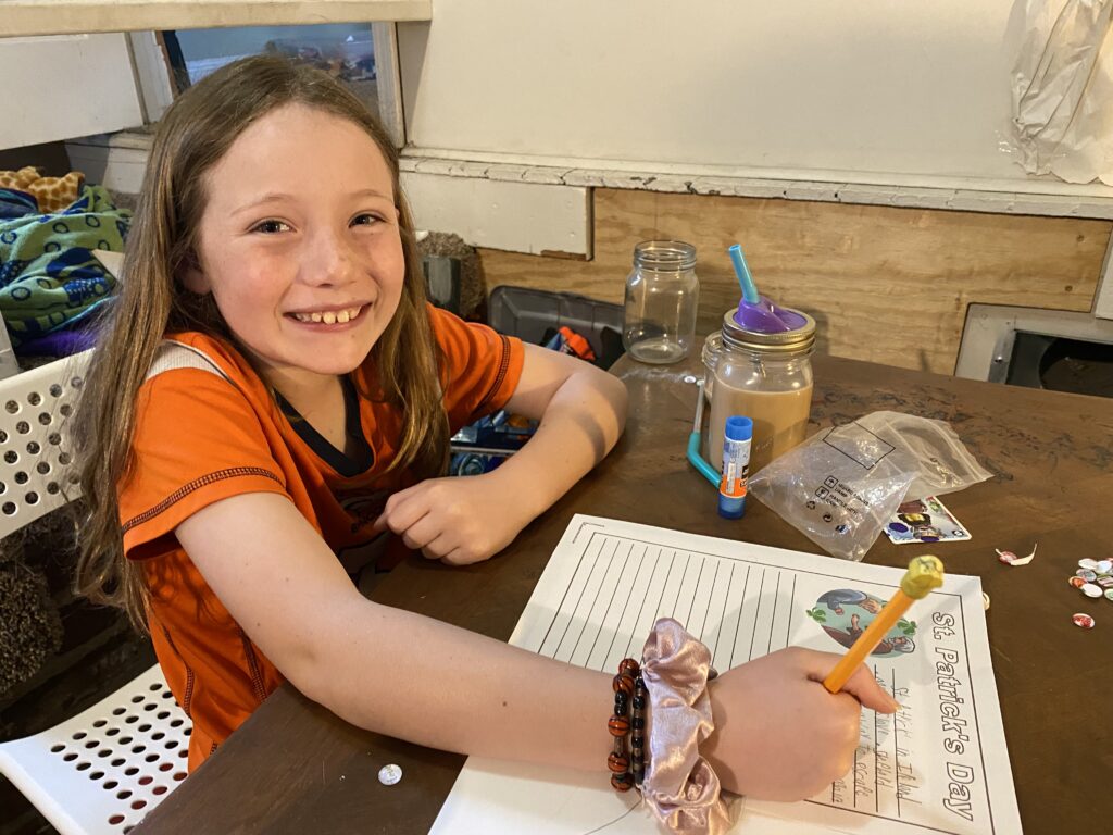 girl sitting at a table with a pencil, writing on a piece of paper for a st. patrick's day unit study.
