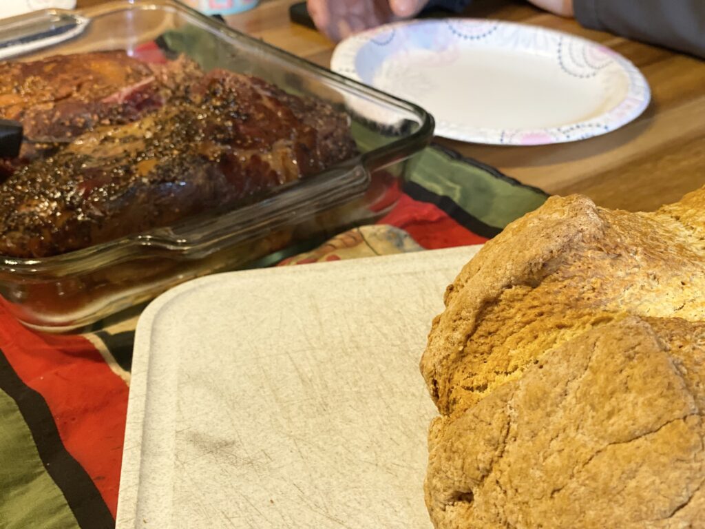 irish soda bread sitting on a cutting board with a pan of corned beef in the background for st. patricks day unit study.